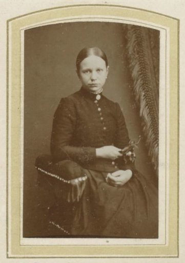 Portrait of a seated woman in a long dress holding a sprig