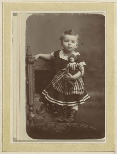 Portrait of a Girl in a Striped Dress Sitting on a Chair with a Doll