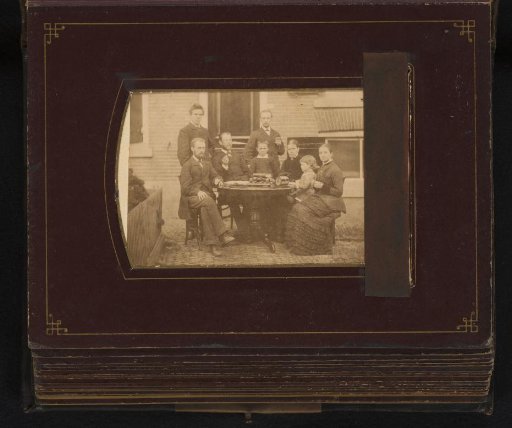 Group portrait of four men, two women and two children around a table in a garden