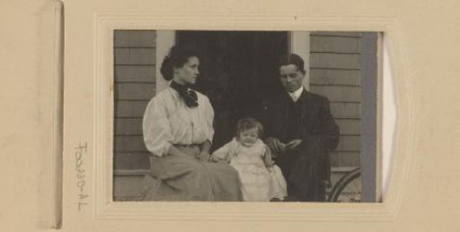 Portrait of a man, woman and child in front of a wooden house