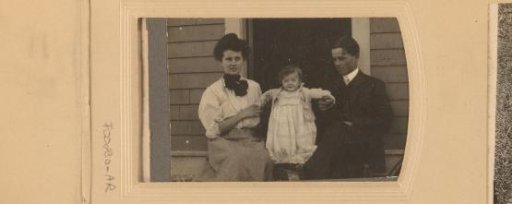 Portrait of a man, woman and child in front of a wooden house