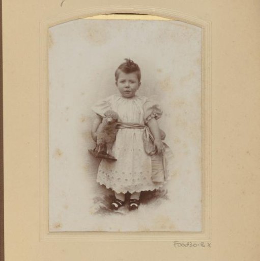 Portrait of a standing toddler in a white dress with a toy sheep