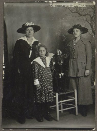 Group portrait of two women with hats, a young girl in a polka-dot dress, and a dog