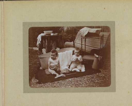 Two toddlers seated on a cloth near a bench and a bath tub, probably the twins Ad and Johanna van der Kop