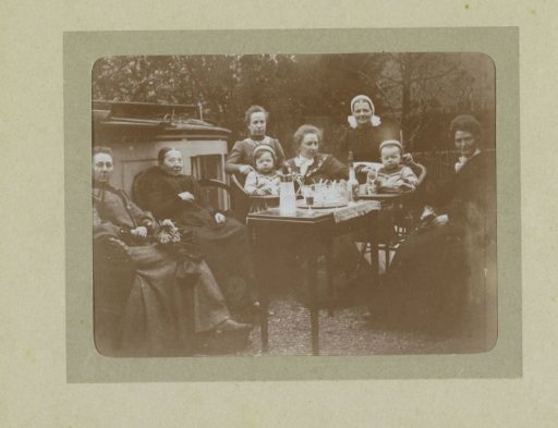 Group portrait of six women and two toddlers in a garden around a table with an advocaat service, probably the twins Ad and Johanna van der Kop, their mother W.G. Hoogendijk and family members