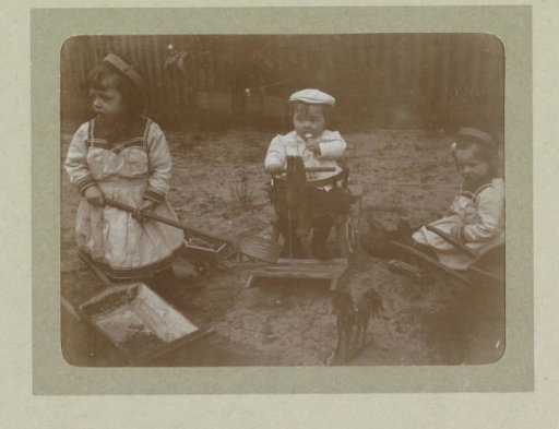 Three toddlers in a garden with toys, a rocking horse and wheelbarrows with a shovel, probably the twins Ad (left) and Johanna (right), and Han (middle) van der Kop