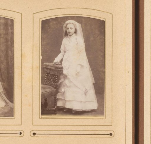 Portrait of a girl in a communion dress, standing by a chair