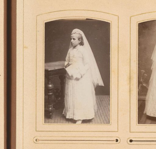 Portrait of a girl in a communion dress, standing by a table with a book in her hand