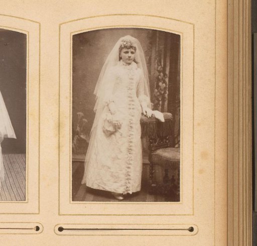 Portrait of a girl in a communion dress, standing by a chair