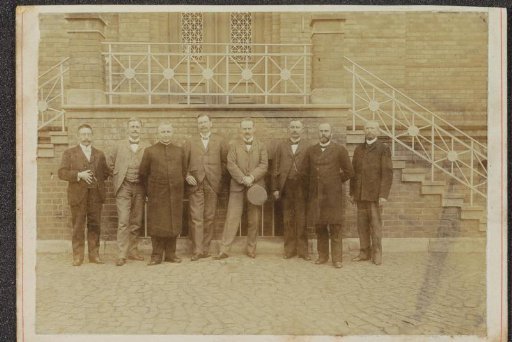 Group portrait of eight men standing before a staircase in Germany