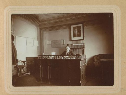 Portrait of a man behind a desk in a room in Germany with a map and an image of Christ on the wall