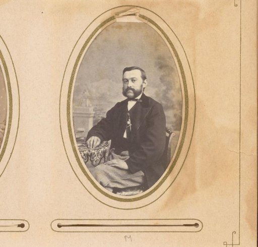 Portrait of a man with a mustache and beard, seated at a table with books