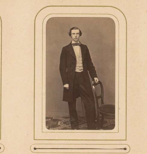 Portrait of a young man with a bow tie, standing by a chair