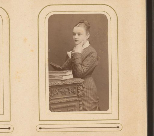 Portrait of a young woman with an open book in hand, standing by a piece of furniture
