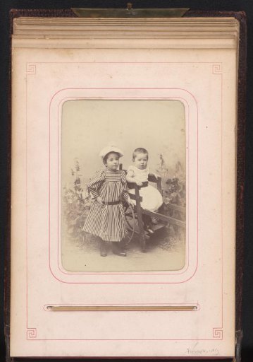 Portrait of two children in a garden setting, a boy in a wooden cart and a girl standing beside him