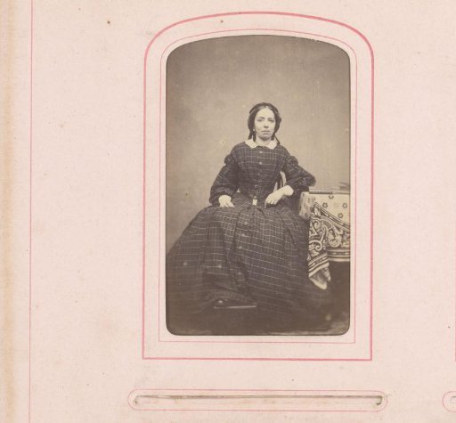 Portrait of a seated woman in a checkered dress, with feet on a stove