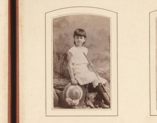 Portrait of a seated girl holding a cane and hat