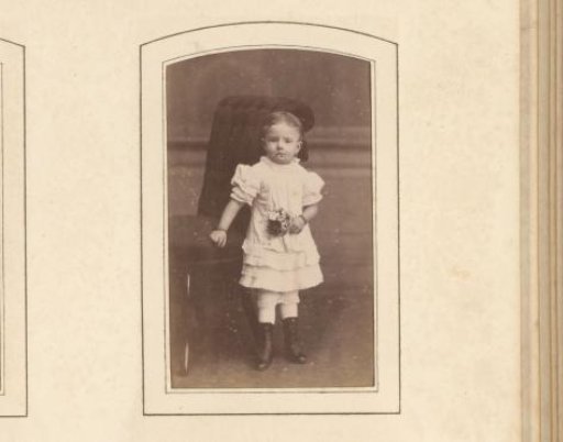 Portrait of a girl with flowers in her hand, standing by a chair