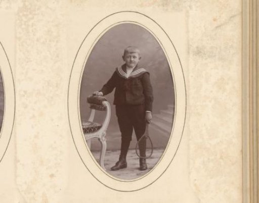 Portrait of a boy with a tennis racket in his hand, standing by a chair
