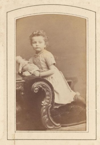 Portrait of a girl with a doll in her hand, kneeling on a chair