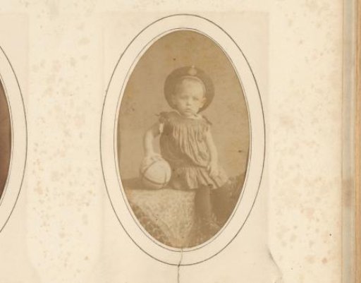 Portrait of a seated girl with a cap and a ball in her hand