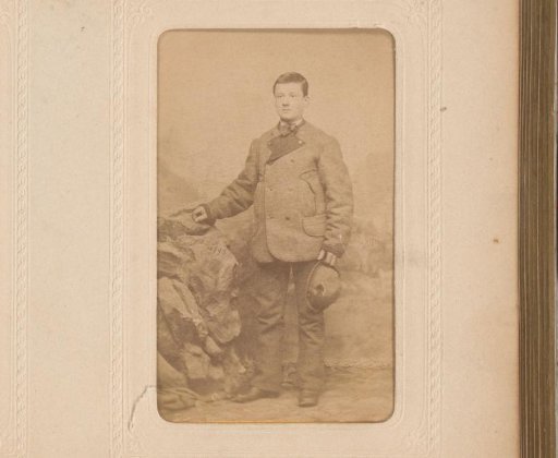 Portrait of a young man with a hat in his hand, standing before a backdrop