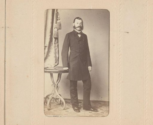 Portrait of a man with a moustache and sideburns, standing by a table