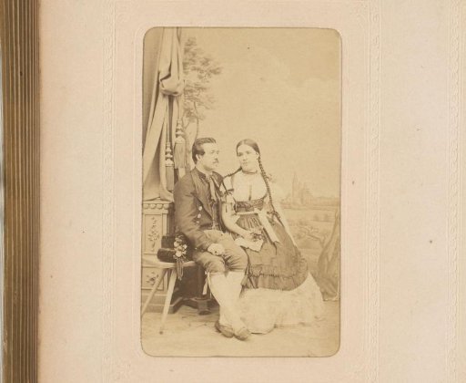 Portrait of a seated man and woman in costume before a backdrop
