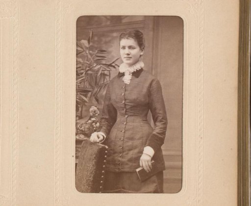 Portrait of a young woman with a book in her hand, standing by a chair