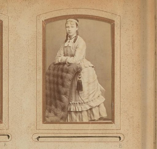 Portrait of a girl with ringlets, standing by a chair