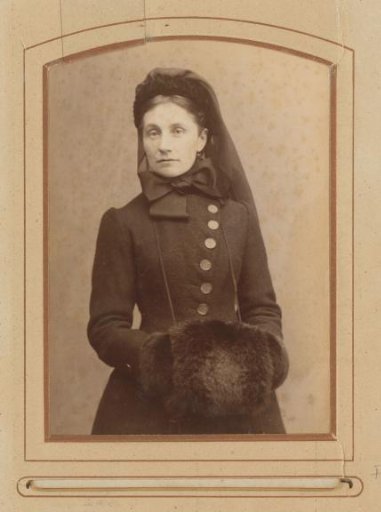 Portrait of a standing woman in a cloak with muff, bow and cap with veil