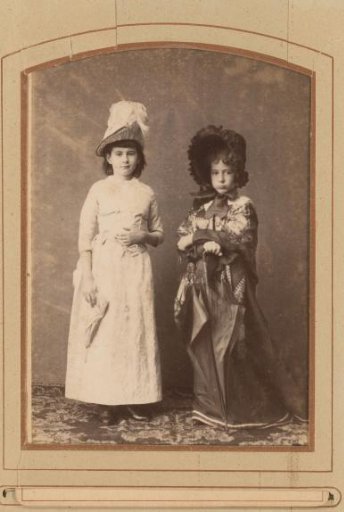 Portrait of two standing girls dressed as ladies, with parasols and hats