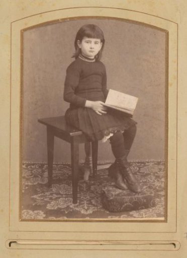 Portrait of a girl with a book in hand, seated on a table