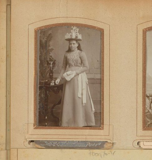 Portrait of a girl with hat, white sash, church book and lace handkerchief, standing by a table with a crucifix