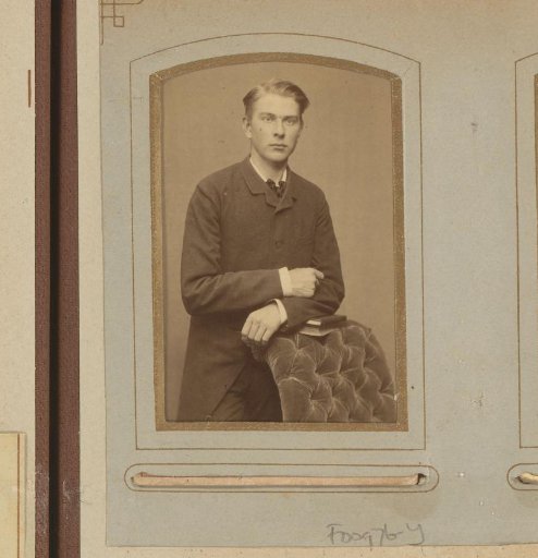 Portrait of a standing man with an overcoat, leaning on books on the arm of an armchair