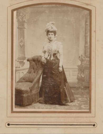 Portrait of a woman with a hat, standing beside a chair