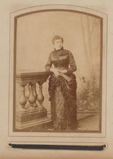 Portrait of a woman with a fan in her hand, standing by a balustrade