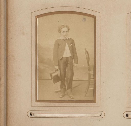 Portrait of a standing boy with a tall hat in his hand