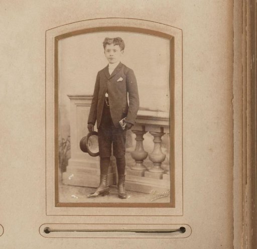 Portrait of a standing boy with a tall hat in his hand