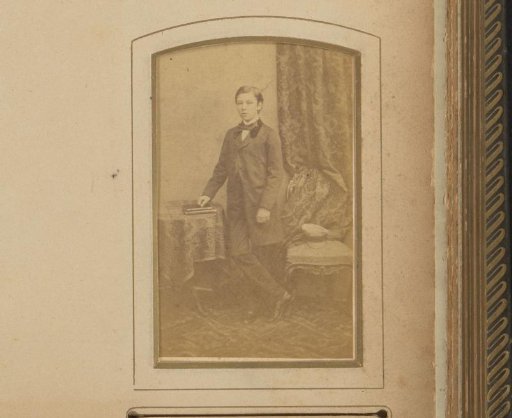 Portrait of a boy in a long coat, standing by a table with books