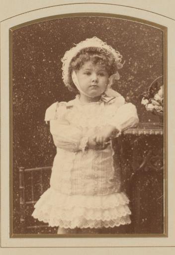 Portrait of a standing girl in a white dress with a cap