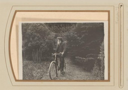 Old man with a white beard and cap on a bicycle on a garden path