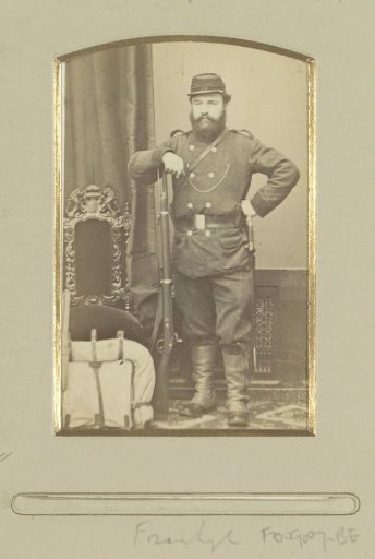 Portrait of a (presumably) French soldier, standing by a knapsack with rifle