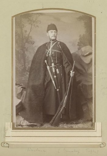 Portrait of a (presumably) Russian military man, standing with a fur cloak, fur cap and weapons
