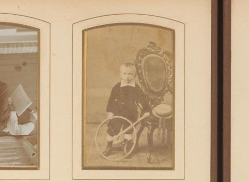 Portrait of a boy with a hoop, standing by a chair with a straw hat