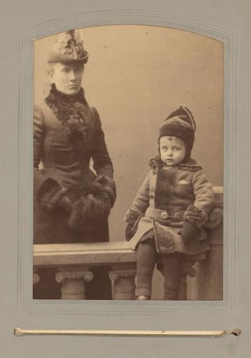 Portrait of a standing woman and a child sitting on a balustrade, dressed in winter clothing