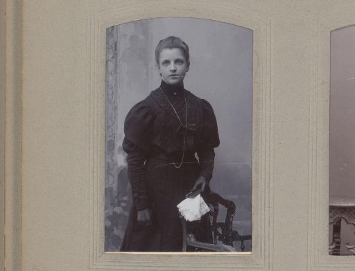 Portrait of a standing young woman in a black dress with a book and white handkerchief in her hand