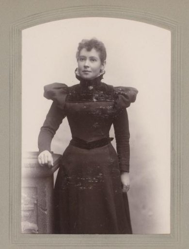 Portrait of a woman in a black dress, standing by a pillar