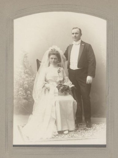Portrait of a married couple in wedding attire, the woman seated and the man standing