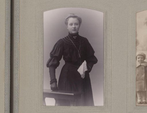 Portrait of a standing young woman, dressed in black with a white handkerchief in her hand